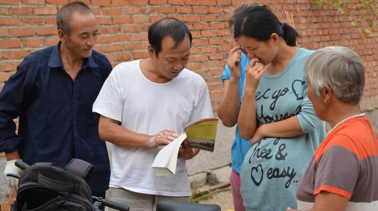 Man with a bike is standing holding a book, four other people looking down at it.